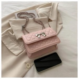 Detail view of pink quilted handbag with silver bow accent and chain strap next to a phone
