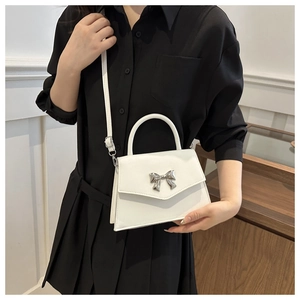 Detailed view of white leather handbag with silver bow metal buckle and thin shoulder strap