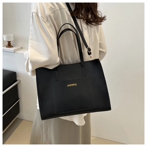Close-up of black matte tote bag featuring gold lettering logo and front pocket detail