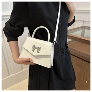 Detail of white leather crossbody bag with a silver metal bow buckle and flip cover