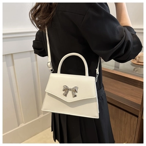 Close-up of a white leather bag with a silver metal bow buckle worn as a crossbody