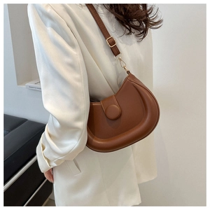 Detail view of a brown crescent shoulder bag with round buckle on a minimalist background