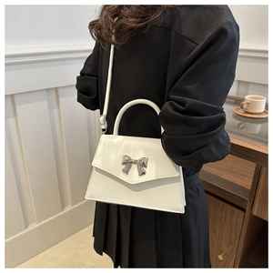 Detail shot of a white crossbody bag featuring a premium silver metal bow ornament