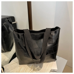 Detail of a black patchwork tote bag with geometric textures and canvas straps on a mirror