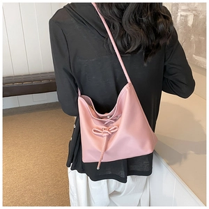 Pink faux leather underarm bag with bow drawstring detail shown on a model