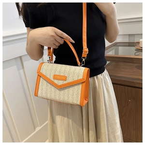 Détail du sac bandoulière en paille avec garniture en cuir orange et lettrage doré