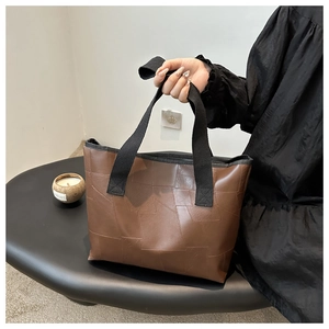 Close-up of brown patchwork faux leather tote bag with black canvas handles and texture