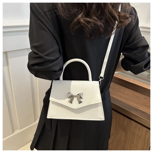 Detailed view of white leather handbag with silver metal bow and top handle strap