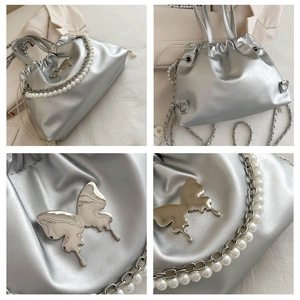 Detail of silver bucket bag with butterfly buckle and pearl chain strap on white blazer