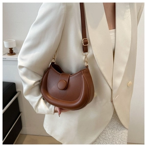Detail of brown matte leather saddle bag with round buckle on white blazer