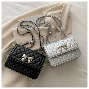 Close-up of quilted crossbody bag with metal chain strap and bow-shaped lock