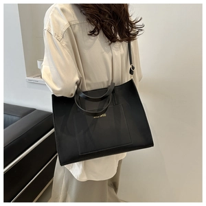 Detail of black leather tote bag showing front pocket and adjustable shoulder strap