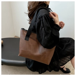 Detail of a brown leather patchwork tote bag with wide strap on a model's shoulder