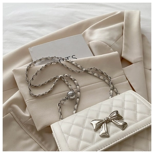Detail of quilted leather handbag with silver bow accent and metal chain strap