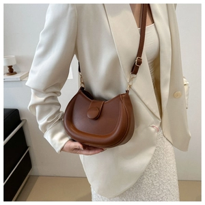 Brown leather crescent shoulder bag with magnetic buckle shown in a lifestyle setting