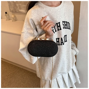 Close-up of black glitter clutch bag with gold bow clasp and metal chain handle