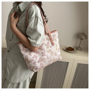 Detail of pink canvas tote bag with butterfly prints and leather strap on model