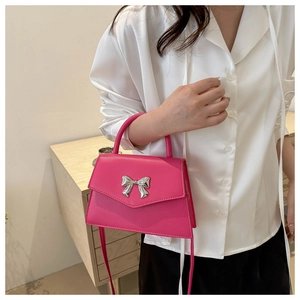 Detail of hot pink crossbody bag with silver bow accent on a white shirt background