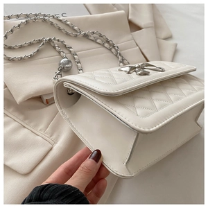 Detail of white quilted leather bag with silver bow ornament and chain strap