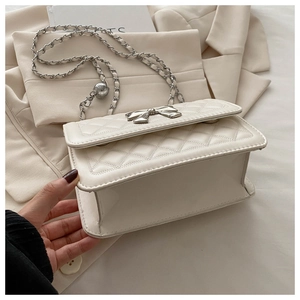 Close-up of white quilted chain bag featuring a large metal bow clasp and adjustable strap