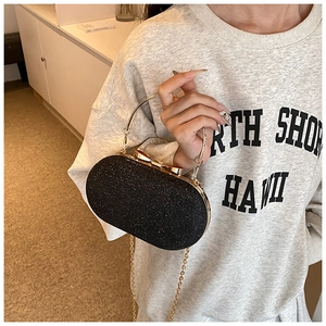 Detail of black sequined clutch bag with gold bow clasp and metallic chain strap