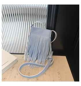 Detail of light blue crossbody bag with long tassels and litchi grain leather texture