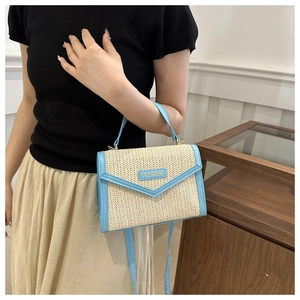 Détail du sac tressé en paille contrastée avec bordure en cuir bleu clair et logo doré