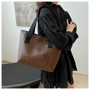 Detail of a brown leather tote bag with a wide black shoulder strap shown on a model