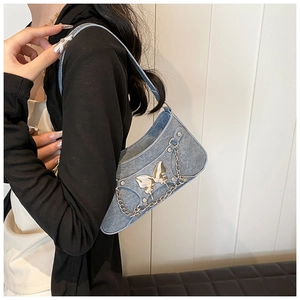 Detalle de bolso de hombro vaquero azul claro con mariposa dorada y cadena de metal