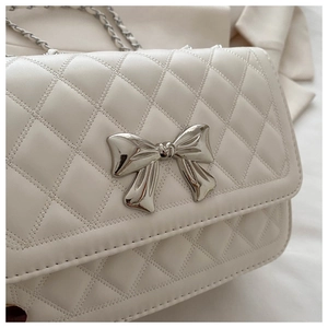 Close-up of white quilted PU leather handbag featuring a silver metal bow buckle detail