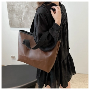 Brown patchwork tote bag with wide black strap shown on a model in a minimalist room