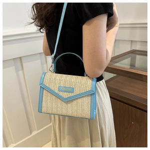 Detail of woven straw handbag with blue leather trim worn crossbody by model