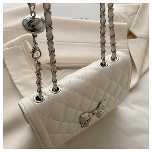 Detail of white quilted leather handbag with silver bow charm and gold ball chain
