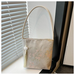 Détail de broderie florale sur un sac seau en soie crème avec de longs glands verts