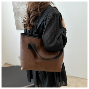 Brown leather tote bag with geometric stitching and wide shoulder strap on model