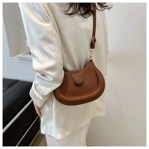Brown leather saddle bag with gold metal buckle shown on a model in a minimalist setting