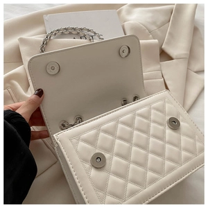 Close-up of white quilted flap bag featuring dual magnetic clasps and silver chain strap