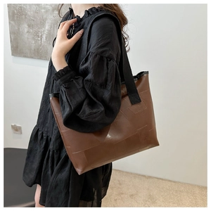 Side view of a brown geometric tote bag with black strap worn with a black dress