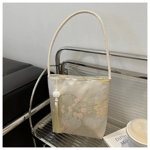 Détail du sac seau en satin avec broderie de fleurs de prunier et pompon jaune
