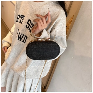Detail of black glitter evening clutch with golden ring handle and bow clasp on gray sweater