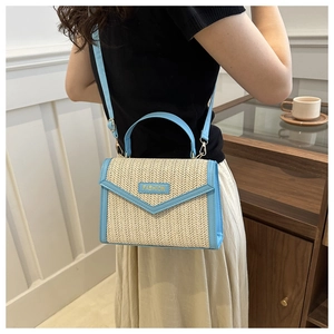Détail du sac à bandoulière en paille avec lanière en cuir bleu et logo doré