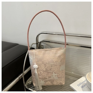 Gros plan d'un sac seau rose en brocart avec motifs de paysages et pompon en soie