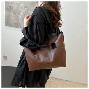 Brown leather tote bag with square patchwork and wide black strap on female model