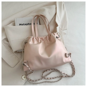 Detail of light pink drawstring bucket bag with pearl handle and chain strap on blazer
