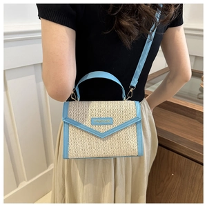 Détail du sac en paille avec garniture bleu clair et plaque tendance sur l'épaule du modèle