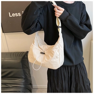 Close-up of cream nylon crossbody bag featuring wrinkled texture and black drawstring detail