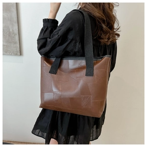 Detailed side view of a brown patchwork leather tote bag with thick black canvas straps