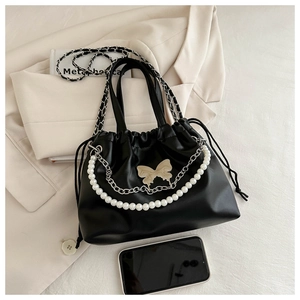 Detail of black drawstring bucket bag featuring pearl handle and butterfly metal ornament
