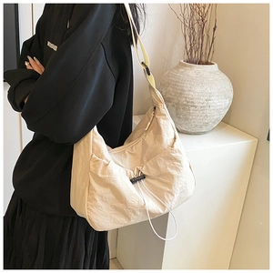 Detail view of cream nylon messenger bag with drawstring and adjustable strap on a model