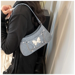 Detalle de bolso de hombro en denim azul con mariposa de metal plateado y tachuelas